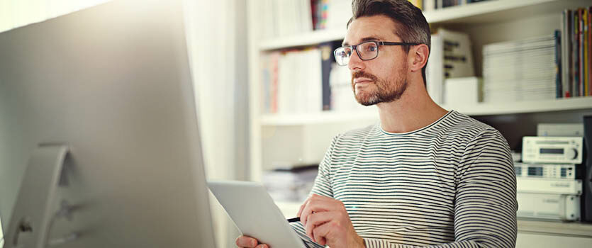 Mann mit Brille arbeitet mit Tablet und Computer