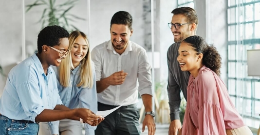 gruppe-menschen-steht-am-schreibtisch-und-schaut-gemeinsam-auf-dokument