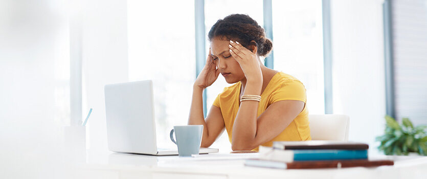 Junge Frau sitzt mit Kopfschmerzen vor ihrem Laptop