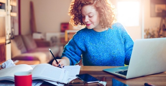Junge Frau im Home-Office notiert sich etwas am Schreibtisch