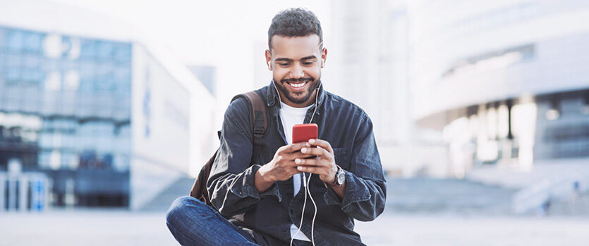 Mann sitzt mit seinem roten Mobiltelefon draußen