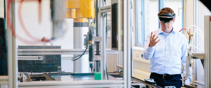 Ingenieur im Hintergrund bedient einen Roboterarm im Vordergrund mit einer VR-Brille