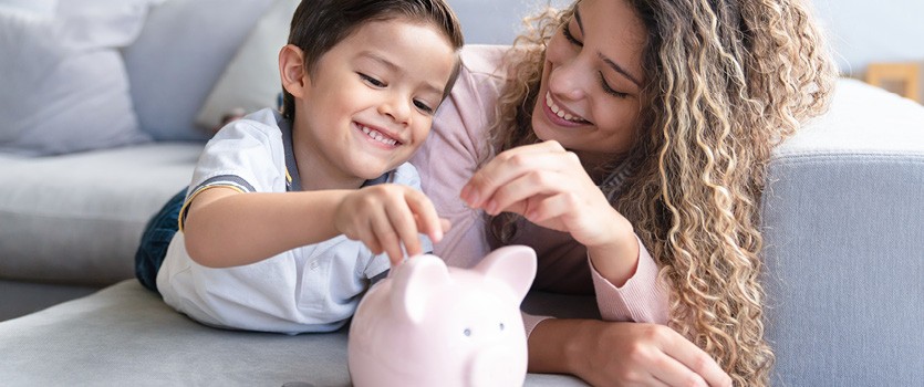 Mutter mit Sohn liegen auf dem Sofa mit einem Sparschwein