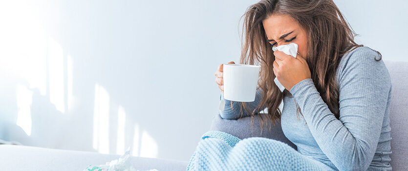 Erkältete Frau sitzt mit einer Tasse Tee auf dem Sofa