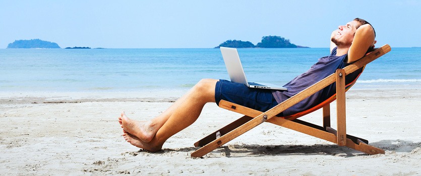 Mann mit Laptop im Liegestuhl am Strand